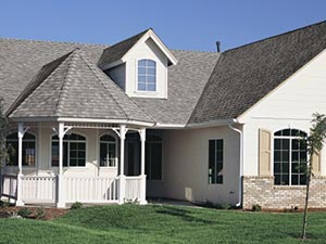 Roof-Leak-Repair-San-Diego-CA-California-1 | Sully-Jones Roofing White suburban house with a covered front porch, gray roof, and a small dormer window on a green lawn.